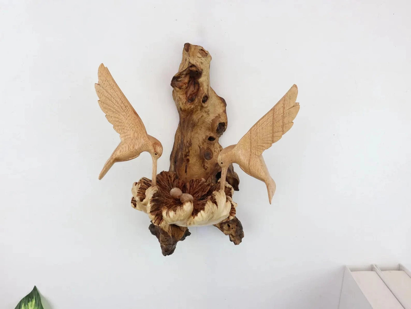 Hand-carved natural wooden wall art featuring a pair of hummingbirds tending to a carved floral nest, with an upright wood log or root base, rustic bird decor.