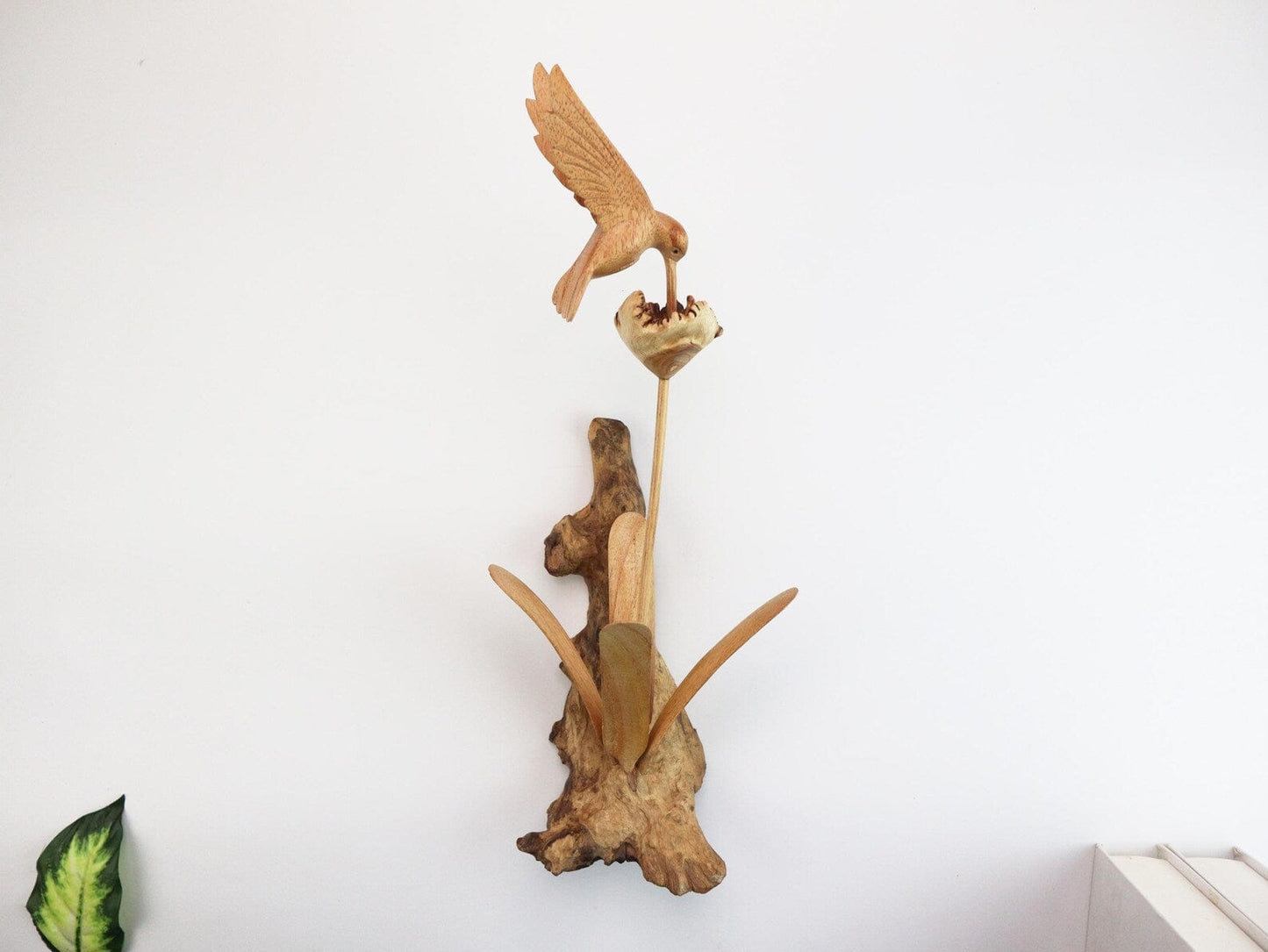 Hand-carved natural wooden wall art featuring a single hummingbird in flight over a flower, with an upright wood log or root base, rustic bird decor.