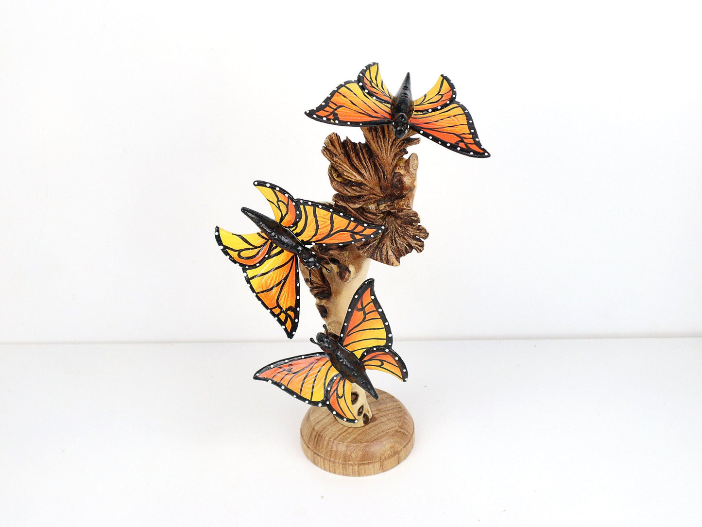 Hand-carved and painted wooden sculpture featuring three vibrant Monarch butterflies on a gnarled upright wood branch, mounted on a round freestanding wooden base, rustic garden decor.