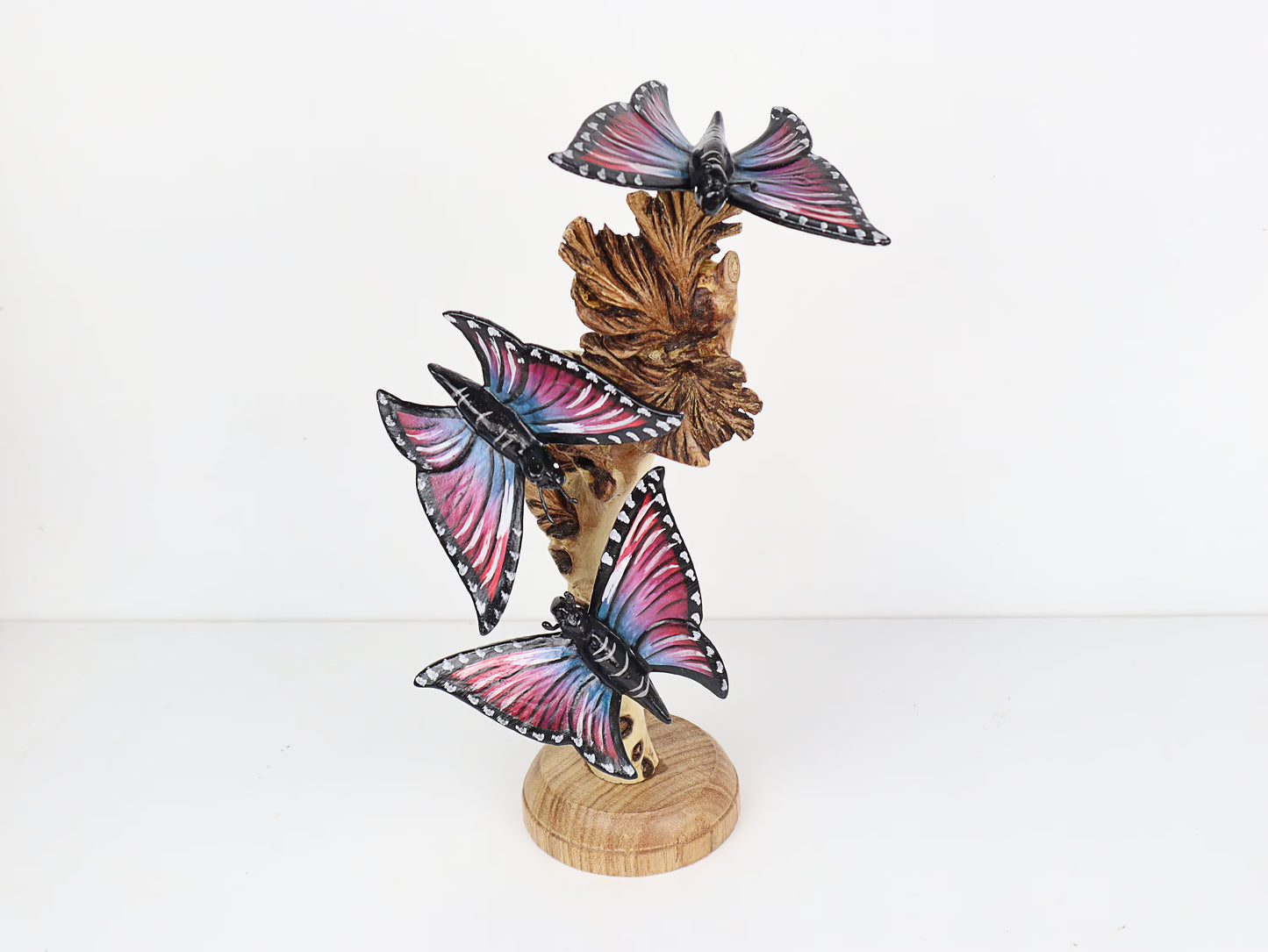 Hand-carved and painted wooden sculpture featuring four multi-colored butterflies on a gnarled upright wood branch, mounted on a round freestanding wooden base, rustic decor.