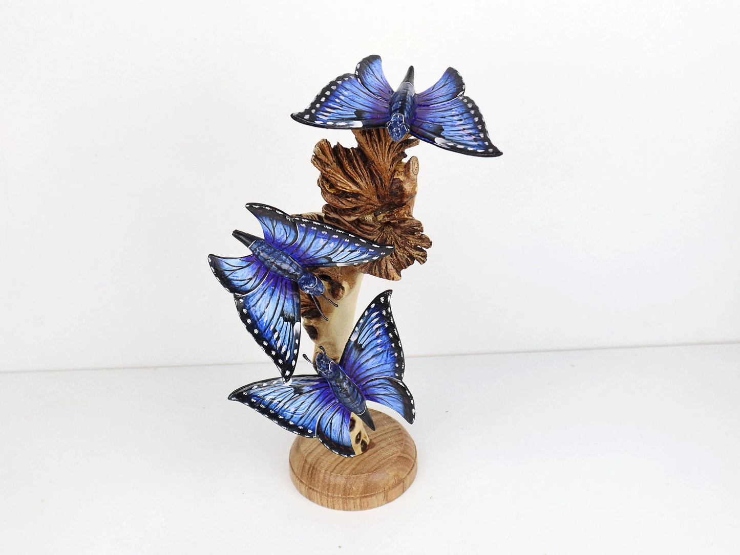 Hand-carved and painted wooden sculpture featuring three vibrant blue butterflies on a gnarled upright wood branch, mounted on a round freestanding wooden base, rustic decor.