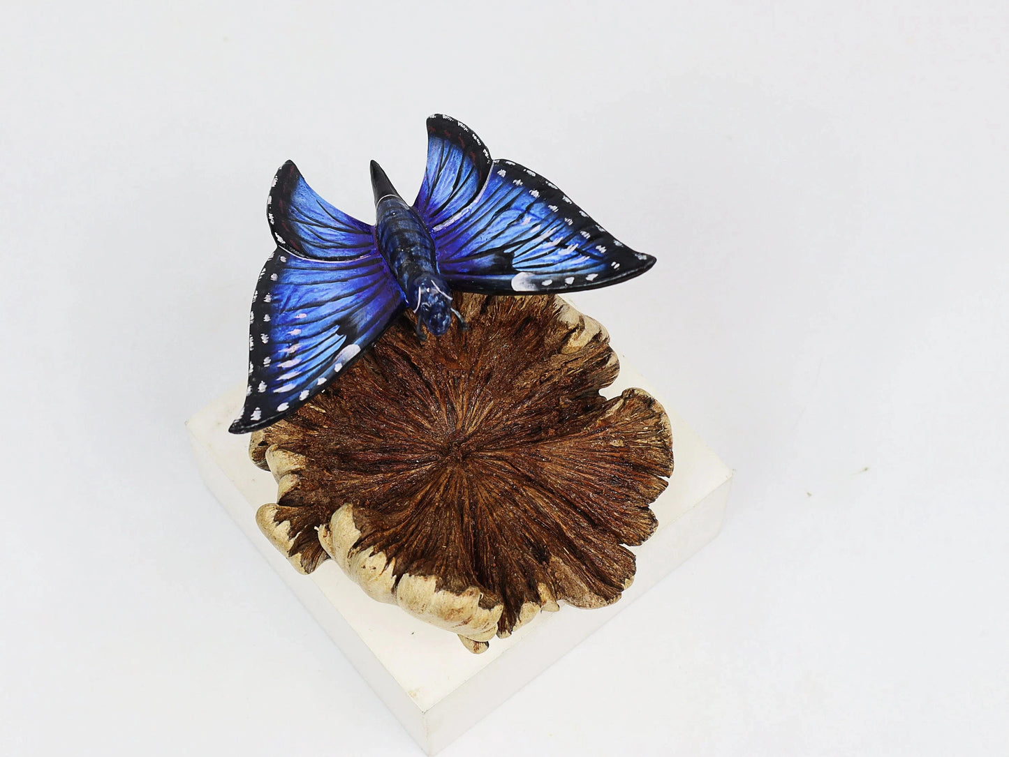 Hand-carved and painted wooden sculpture featuring a blue butterfly on a textured pine cone, mounted on a round freestanding wooden base, rustic insect decor.