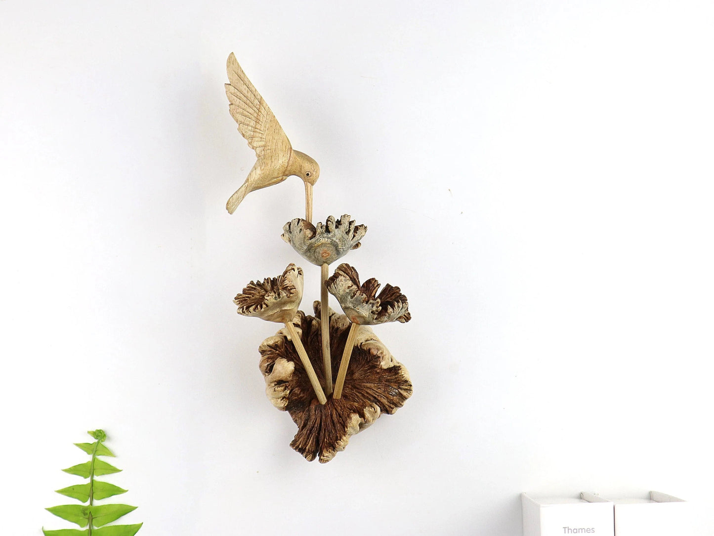 Hand-carved natural wooden wall art featuring a single hummingbird in flight over a cluster of flowers, with an upright wood log or root base, rustic bird decor.