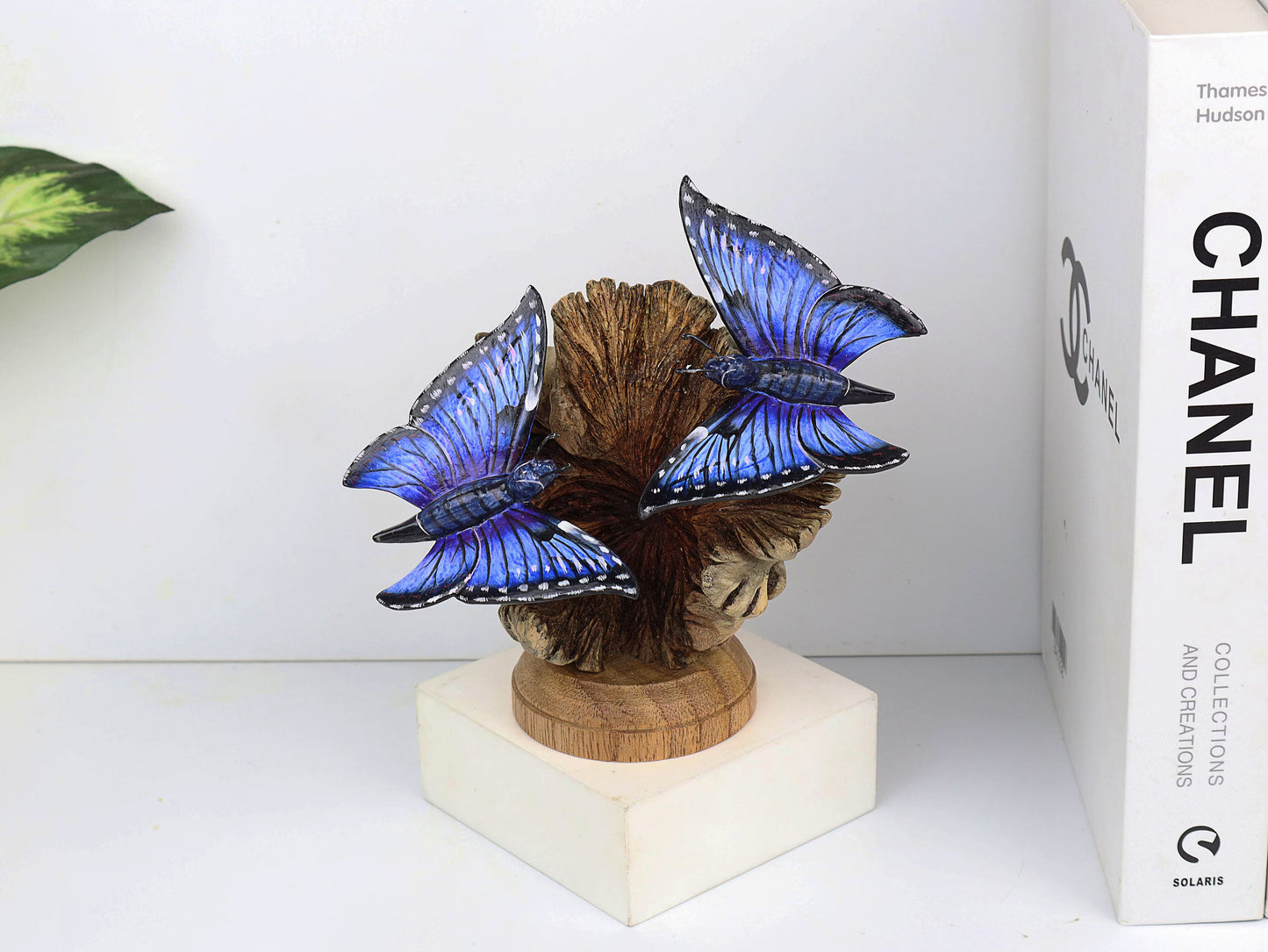 Hand-carved and painted wooden sculpture featuring two vibrant blue butterflies on a gnarled upright wood branch, mounted on a round freestanding wooden base, rustic decor.