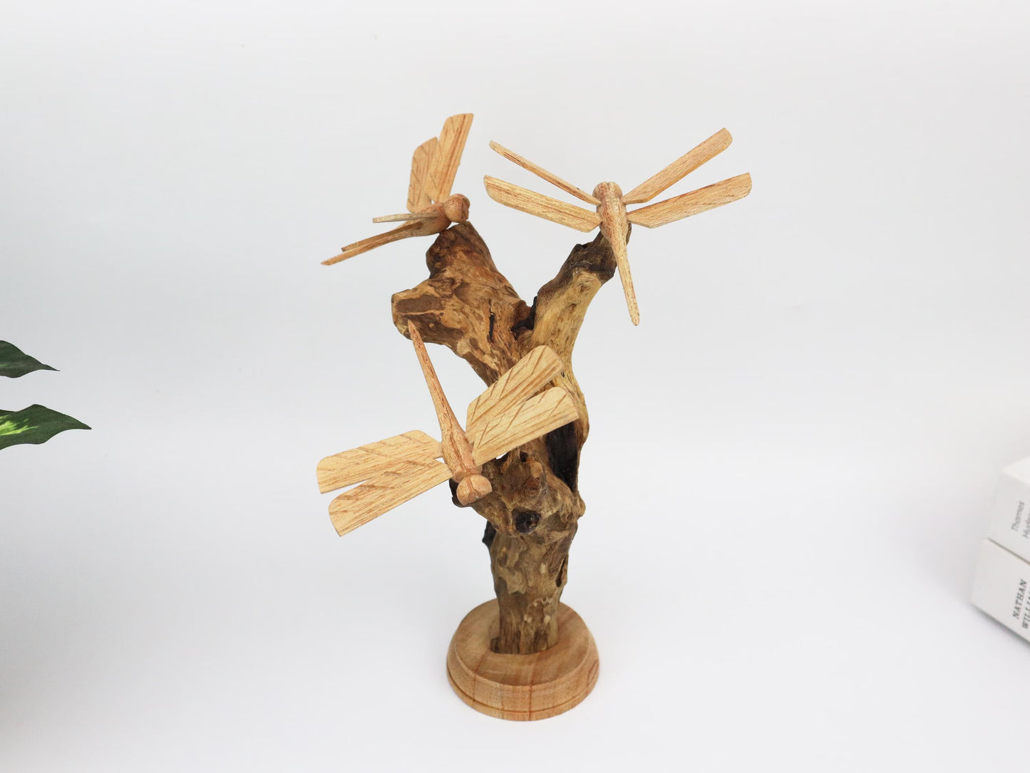 Hand-carved natural wooden sculpture featuring three dragonflies interacting with a gnarled upright wood base, mounted on a round freestanding wooden base, rustic tabletop decor.