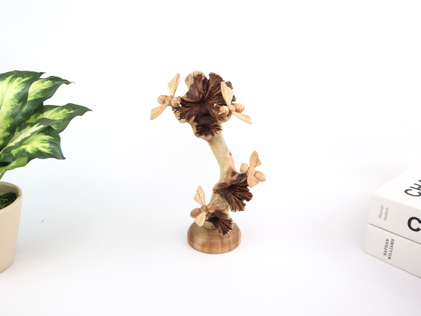 Hand-carved natural wooden sculpture featuring four unpainted bees on a vertical branch with a dark seed pod, mounted on a round freestanding wooden base, rustic nature decor.