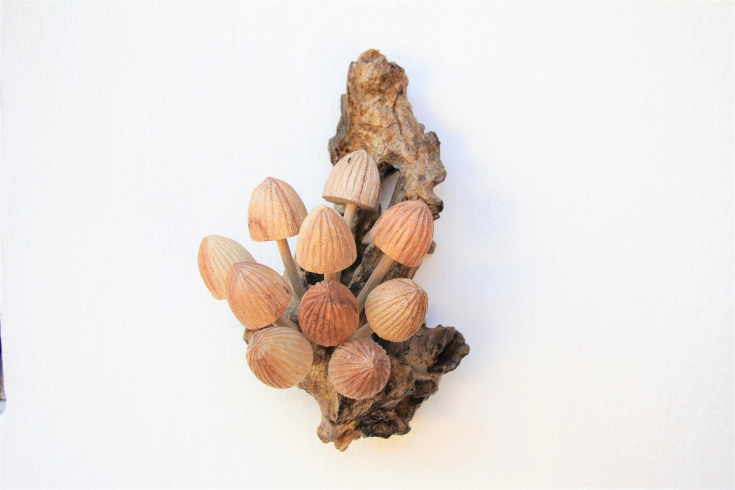 Vertical hand-carved natural wooden sculpture featuring multiple conical mushrooms with prominent ridged caps fanning out along an upright wood log or root, rustic wall art decor.
