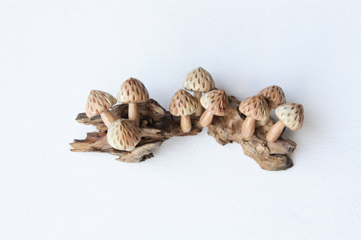 Hand-carved natural wooden sculpture featuring multiple mushrooms with textured caps growing horizontally on a rustic wood log or root, rustic woodland decor.