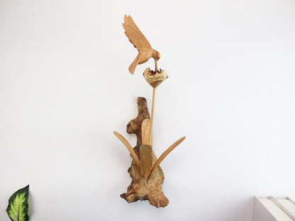 Hand-carved natural wooden wall art featuring a single hummingbird in flight over a flower, with an upright wood log or root base, rustic bird decor.