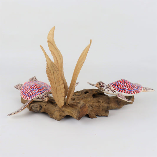 Hand-carved and painted wooden sculpture featuring a pair of sea turtles with red, white, and blue shells, swimming around a central seaweed-like wood carving on a rugged driftwood base, colorful coastal decor.