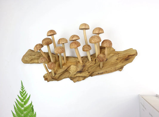 Large hand-carved natural wooden sculpture featuring a dense cluster of multiple mushrooms with textured caps growing horizontally on a substantial wood log or root, rustic forest display.