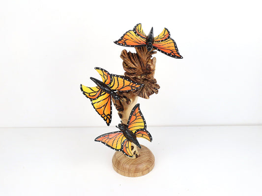 Hand-carved and painted wooden sculpture featuring three vibrant Monarch butterflies on a gnarled upright wood branch, mounted on a round freestanding wooden base, rustic garden decor.