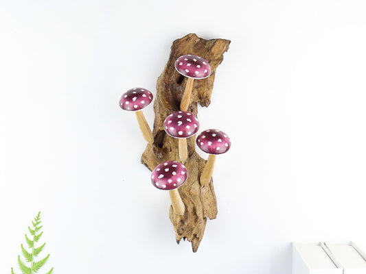 Hand-carved natural wooden wall art featuring five pink and purple polka-dot mushrooms on an upright natural wood log or root, whimsical fairy tale decor.