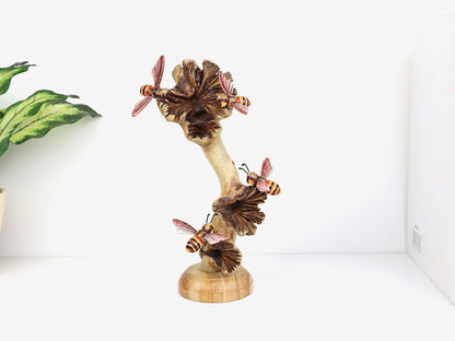 Hand-carved and painted wooden sculpture featuring four bees with orange and black striped bodies on mushroom-like elements, on a rustic wood base, tabletop decor.