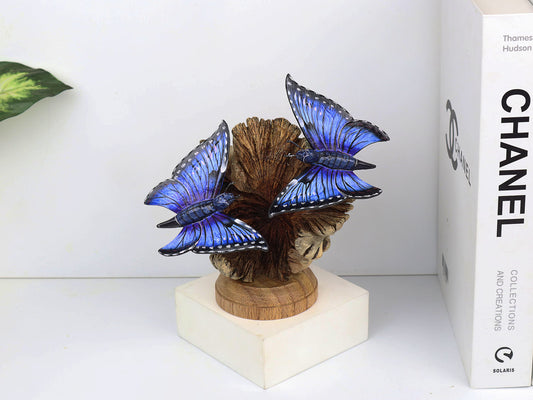 Hand-carved and painted wooden sculpture featuring two vibrant blue butterflies on a gnarled upright wood branch, mounted on a round freestanding wooden base, rustic decor.