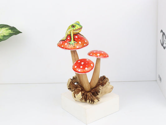 Hand-carved wooden mushroom sculpture with a green frog perched on a red and white polka-dot mushroom, on a rustic wood base, whimsical tabletop decor.