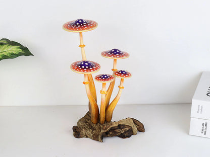 Hand-carved wooden mushroom sculpture with a cluster of five orange and purple caps with white polka dots and long stems on a rustic wood base, whimsical tabletop decor.