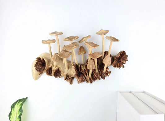 Hand-carved natural wooden sculpture featuring multiple fanned and pleated mushrooms growing horizontally on a low, rugged wood log or root, rustic tabletop centerpiece.