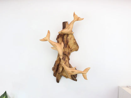 Hand-carved natural wooden wall art featuring three dolphins leaping from a rugged driftwood base, rustic coastal decor.