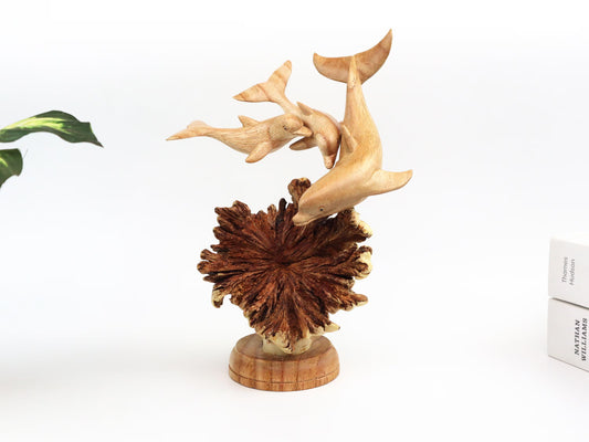 Hand-carved natural wooden sculpture featuring a dolphin family (three dolphins) on a large, textured seed pod base, rustic coastal decor.
