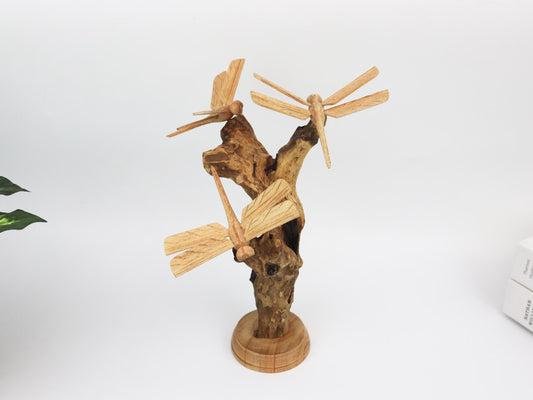 Hand-carved natural wooden sculpture featuring three dragonflies interacting with a gnarled upright wood base, mounted on a round freestanding wooden base, rustic tabletop decor.