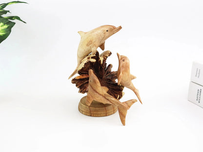 Hand-carved natural wooden sculpture featuring a dolphin family (three dolphins) on a large, textured seed pod base, rustic coastal decor.