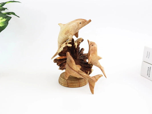 Hand-carved natural wooden sculpture featuring a dolphin family (three dolphins) on a large, textured seed pod base, rustic coastal decor.