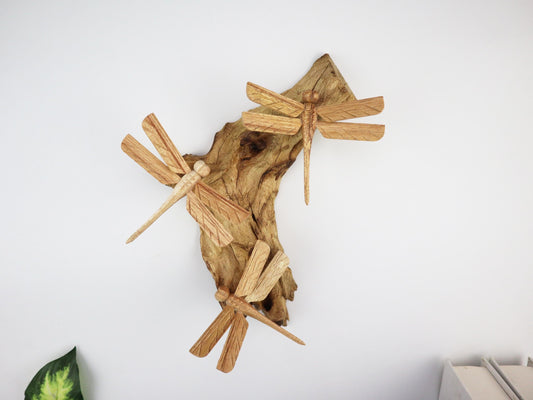 Hand-carved natural wooden wall art featuring three dragonflies interacting with a gnarled upright wood base, rustic woodland decor.