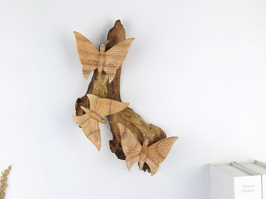Hand-carved natural wooden wall art featuring three large butterflies fluttering vertically on a textured wood log or root, rustic woodland decor.